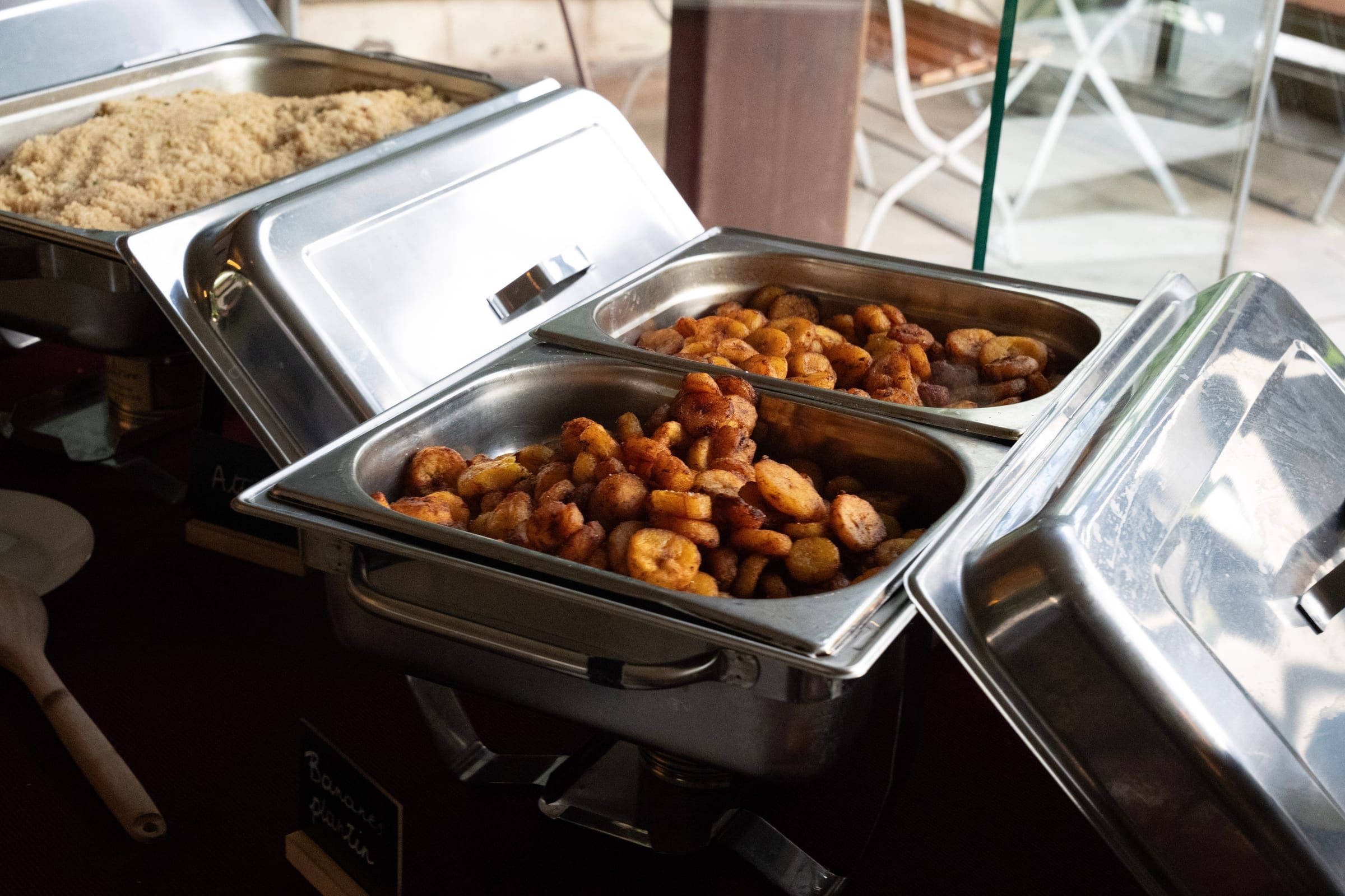 Bananes plantain frites servies dans des chauffe-plats lors d’un buffet, avec une semoule à l’arrière-plan.