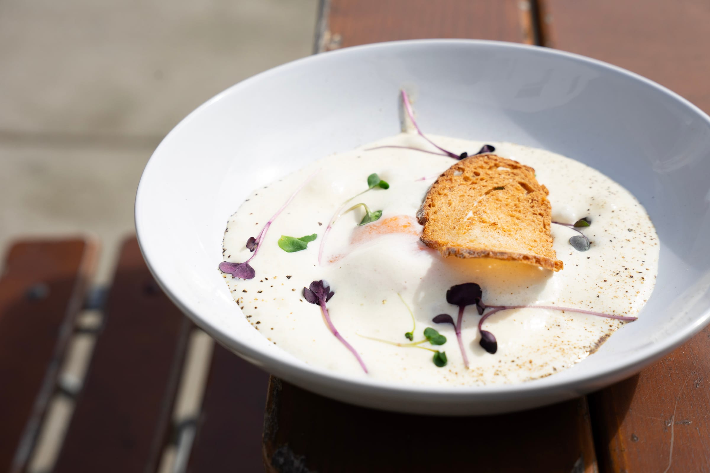 Velouté crémeux parsemé de jeunes pousses, avec un croûton doré, dans une assiette creuse blanche.